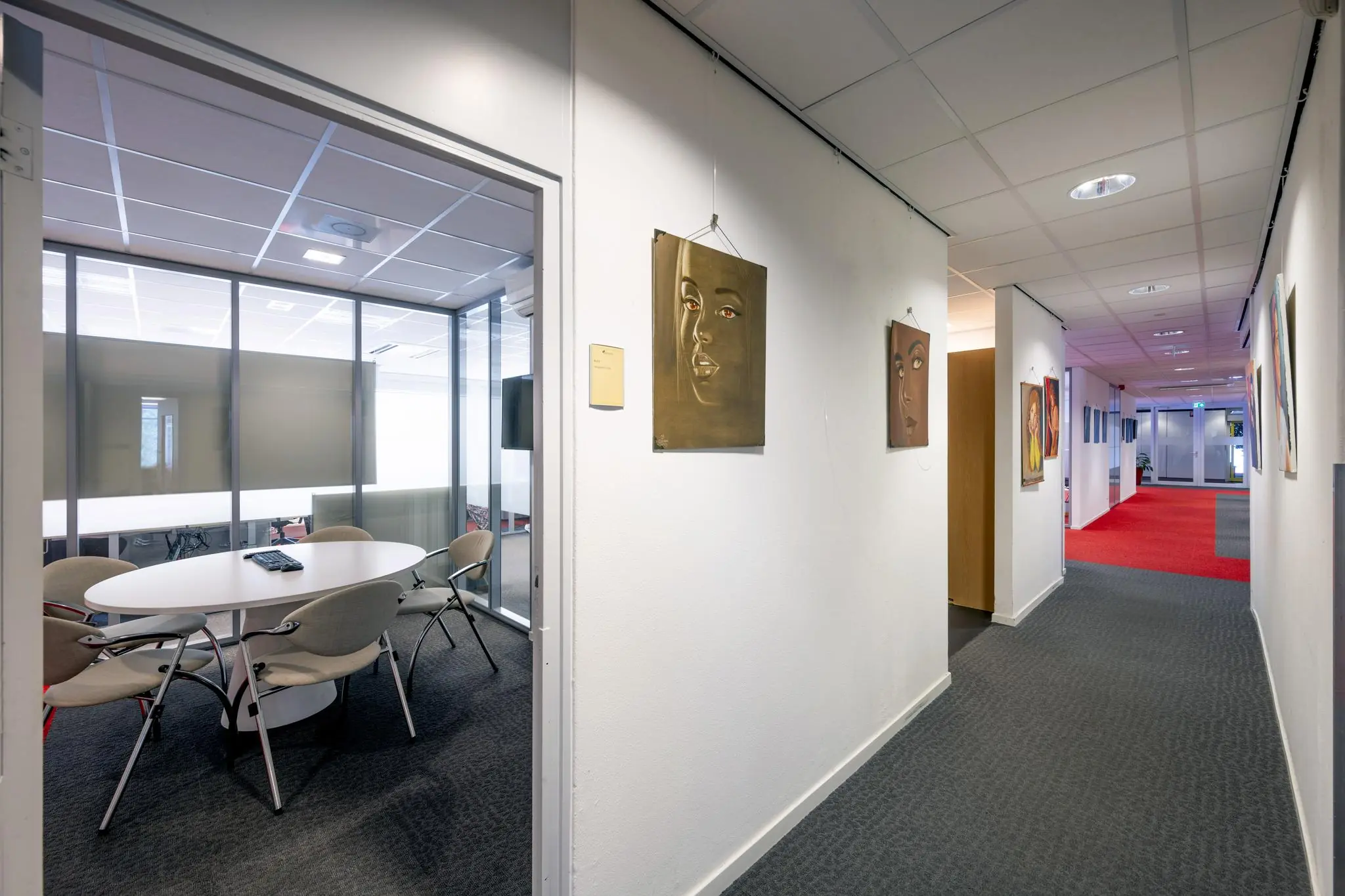 Gang in een kantoorgebouw aan de Jan Tooropstraat met kunst aan de muur en een vergaderruimte links.